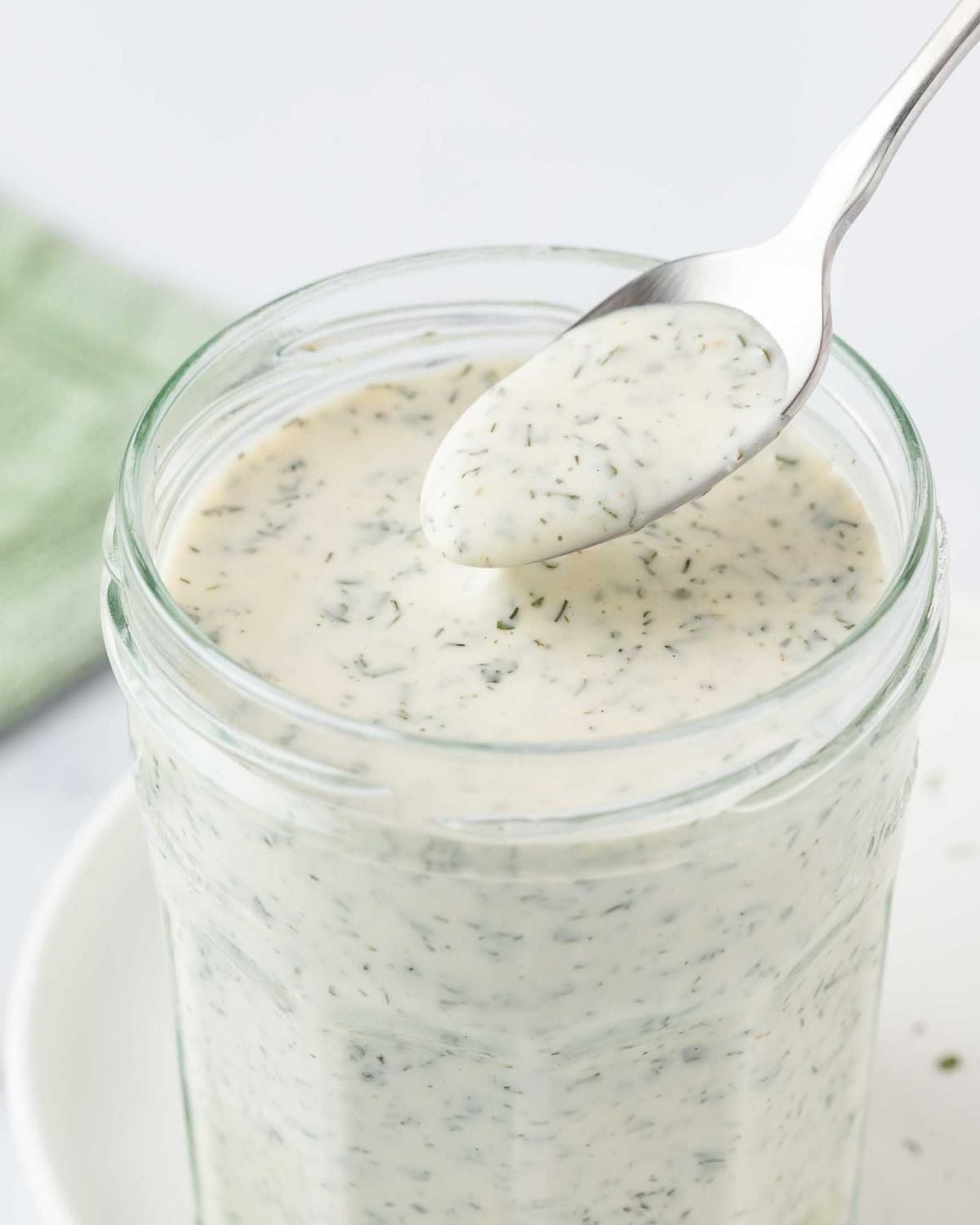 homemade ranch dressing stored in a mason jar. A spoon is lifting some of the ranch dressing to show the thickness