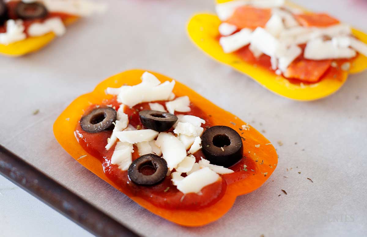 image: orange, red, yellow and green bell pepper pizzas on a baking sheet before baking.