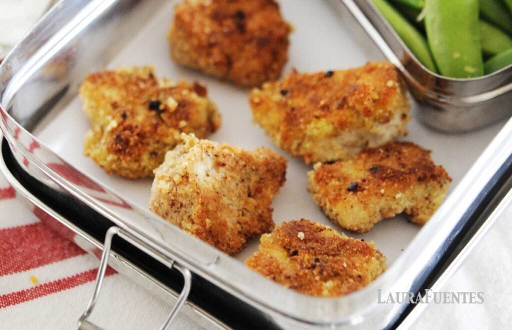 lunchbox with six chicken nuggets and veggies on the side.