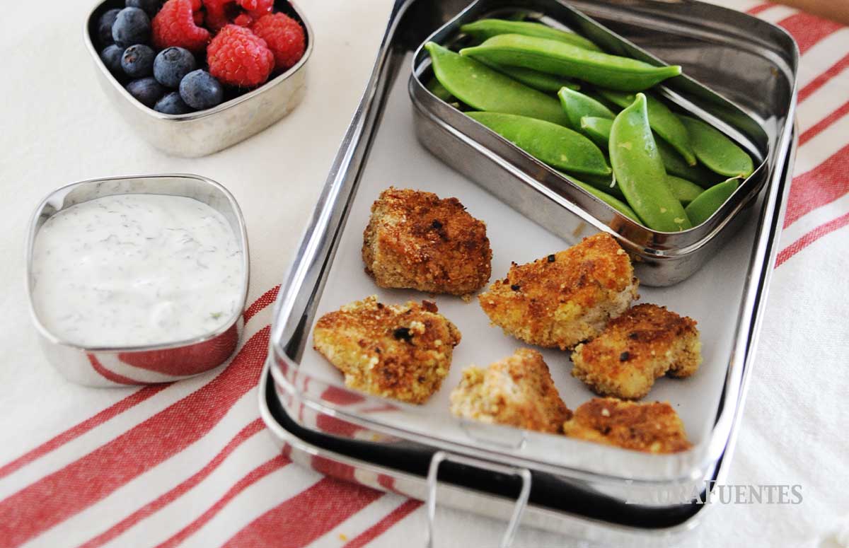lunchbox with six chicken nuggets and veggies on the side, a mini sauce container with a dip and anothe small container with berries.