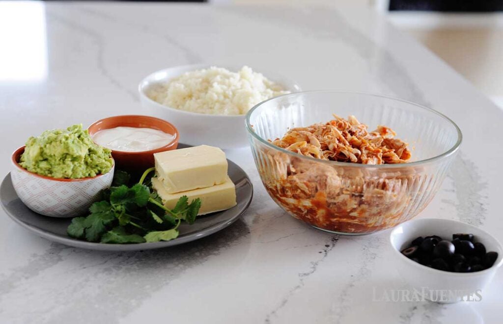 bowls with salsa chicked, riced cauliflower, olives, guacamole, sour cream, cheese, and cilantro