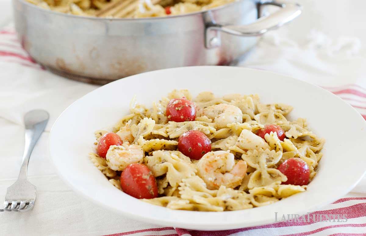 Bowl of shrimp pesto pasta with tomatoes, in front of a skillet full of the pasta