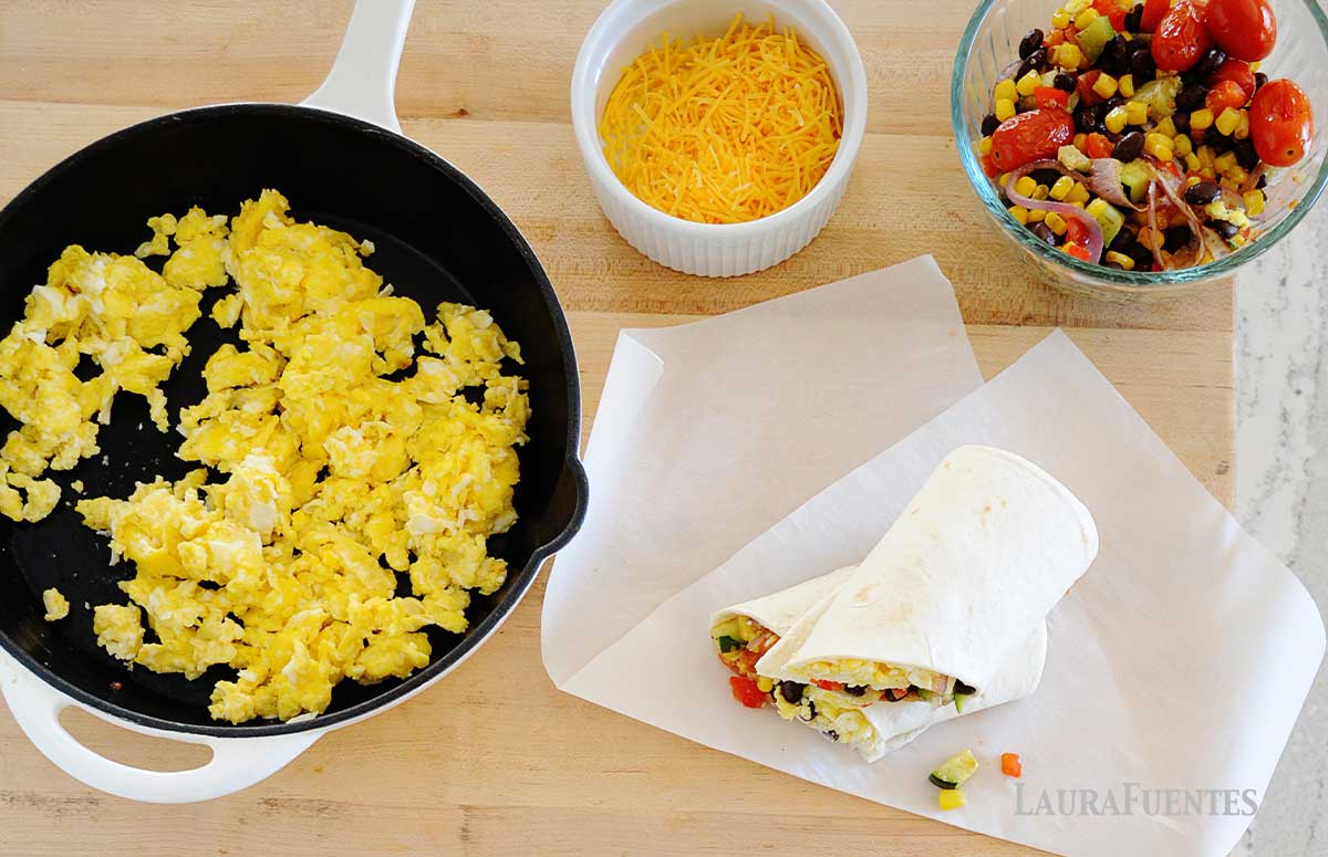 overhead view of breakfast burritos, scrambled eggs in a pan, and shredded cheese