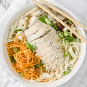 image: overhead view of udon soup with sliced chicken, green peppers and chopsticks.