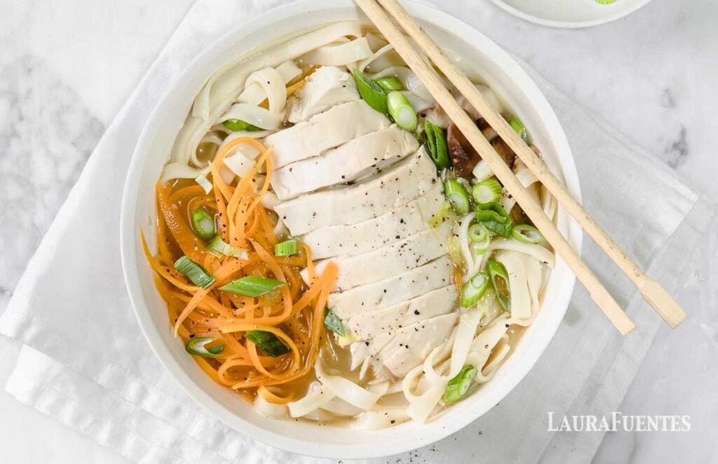image: bowl of udon soup with sliced chicken breast on top. Served with chopsticks.