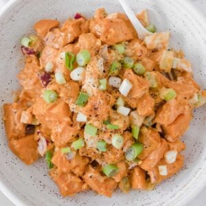 image: overhead view of sweet potato salad ingredients in a bowl. Diced sweet potatoes, chopped boiled egg, green onions, purple onion and creamy dressing.