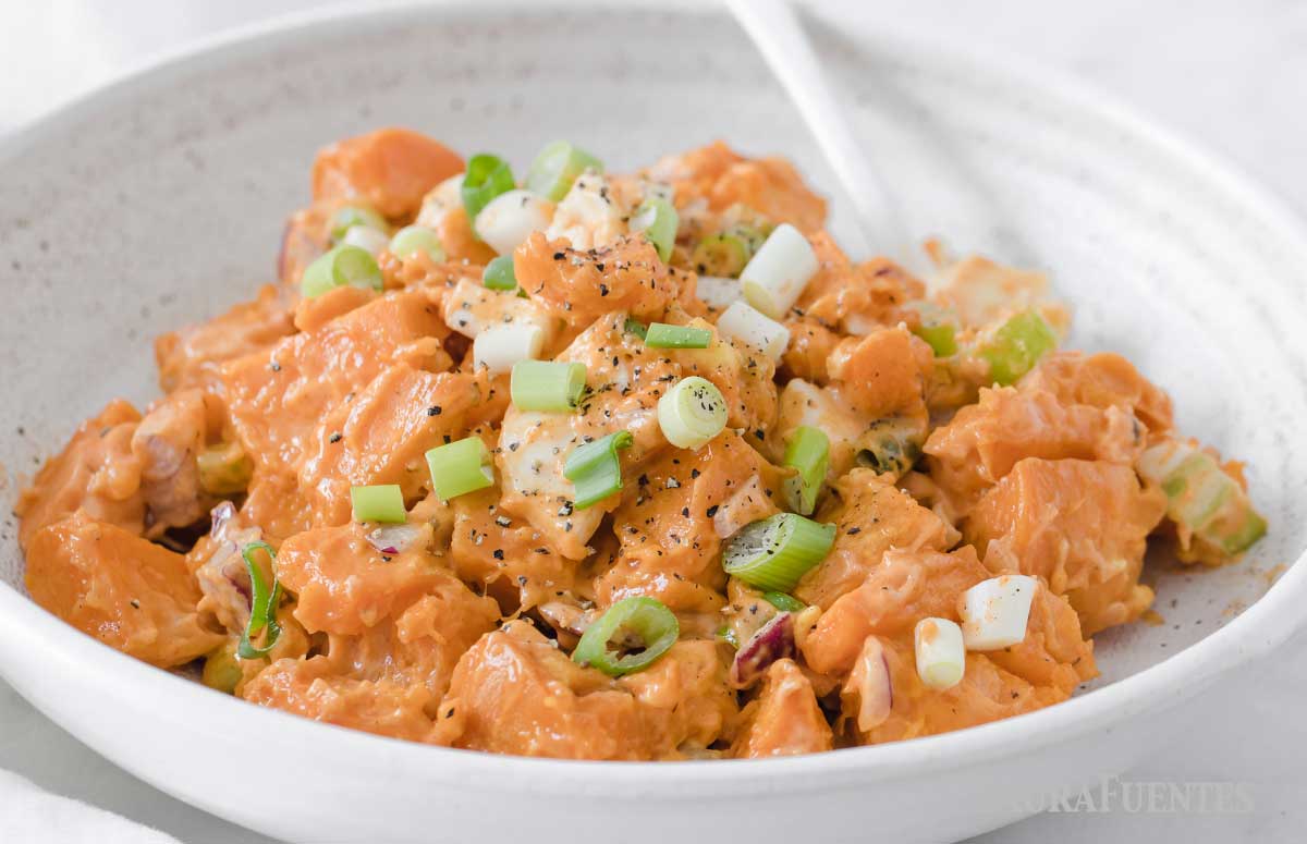 image: closeup view of sweet potato salad ingredients in a bowl. Diced sweet potatoes, chopped boiled egg, green onions, purple onion and creamy dressing.