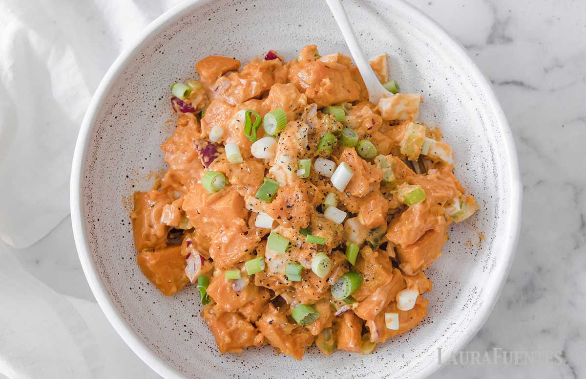 image: overhead view of sweet potato salad ingredients in a bowl. Diced sweet potatoes, chopped boiled egg, green onions, purple onion and creamy dressing.