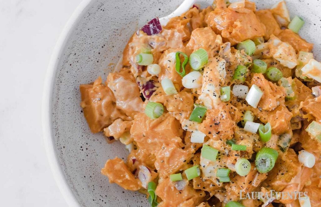 image: overhead view of sweet potato salad ingredients in a bowl. Diced sweet potatoes, chopped boiled egg, green onions, purple onion and creamy dressing.