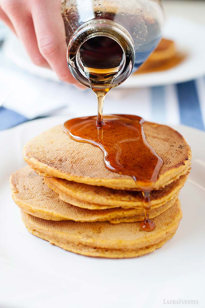 image: stack of pumpkin pancakes on a plate - maple syrup being poured over the top.