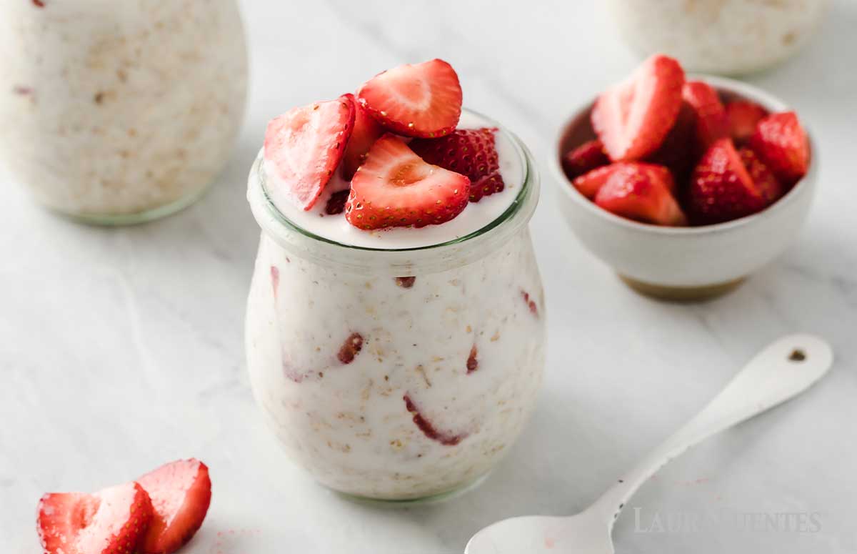 three small glass jars filled to the brim with overnight oats and sliced strawberries