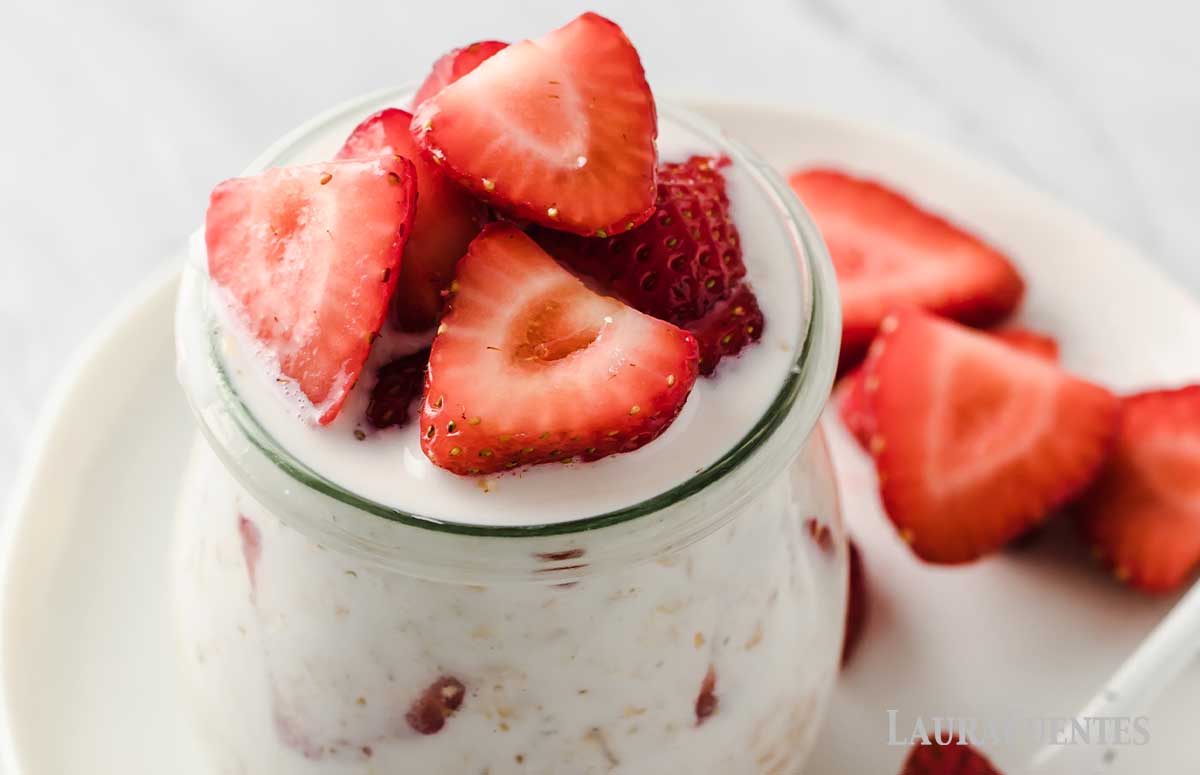 small glass jar filled with overnight oats and sliced strawberries. Additional sliced strawberries to the side on the plate