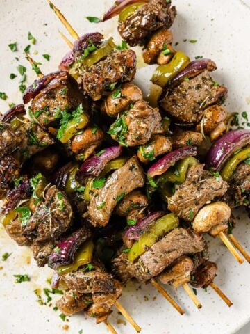 overhead view of delicious marinated grilled beef kabobs on a plate. Beef skewers also have onions and mushrooms
