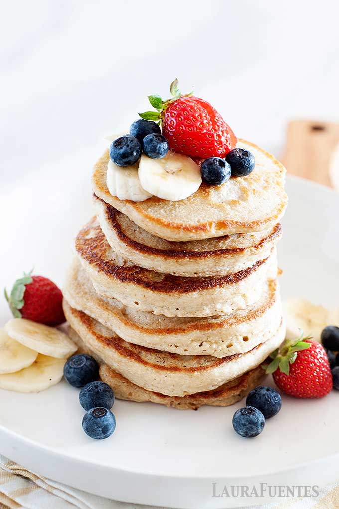 image: closeup of pancake stack with berries and sliced bananas on top and surrounding the stack.
