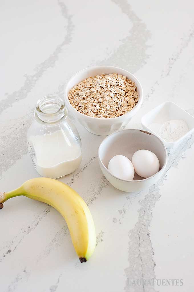 image: flatlay of ingredients for banana oatmeal pancakes. Oats, almond milk, eggs, banana, baking powder and salt