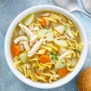 overhead view of a bowl of rotisserie chicken noodle soup with chicken noodles and carrots. some bread on side