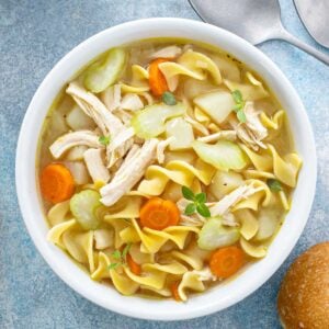 overhead view of a bowl of rotisserie chicken noodle soup with chicken noodles and carrots. some bread on side