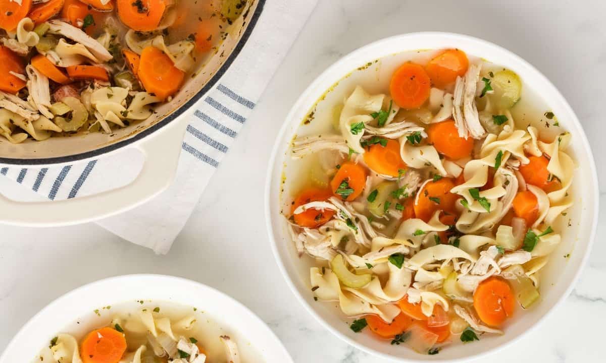 two bowls of rotisserie chicken noodle soup next to a large pot of soup