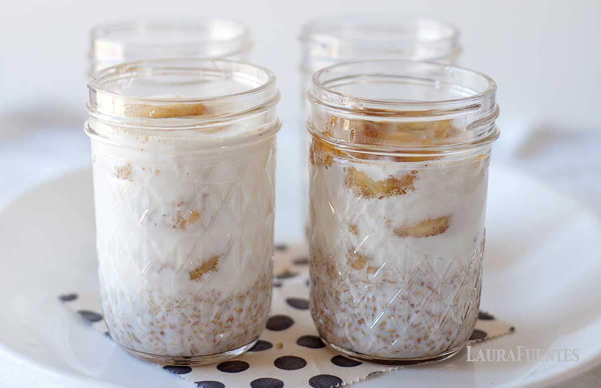 four mason jars on a plate filled with bananas foster overnight oats with steel cut oats