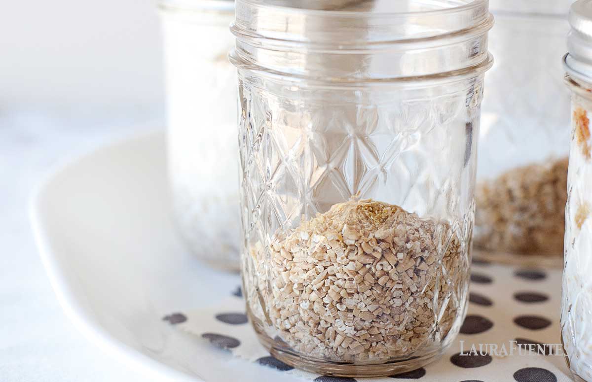 four mason jars on a plate, one is in the foreground filled with oats