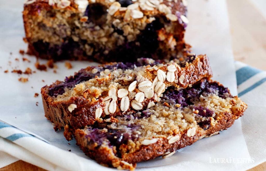 image: closeup view of breakfast bread loaf with blueberries and topped with oats. Two slices cut in front of the loaf.