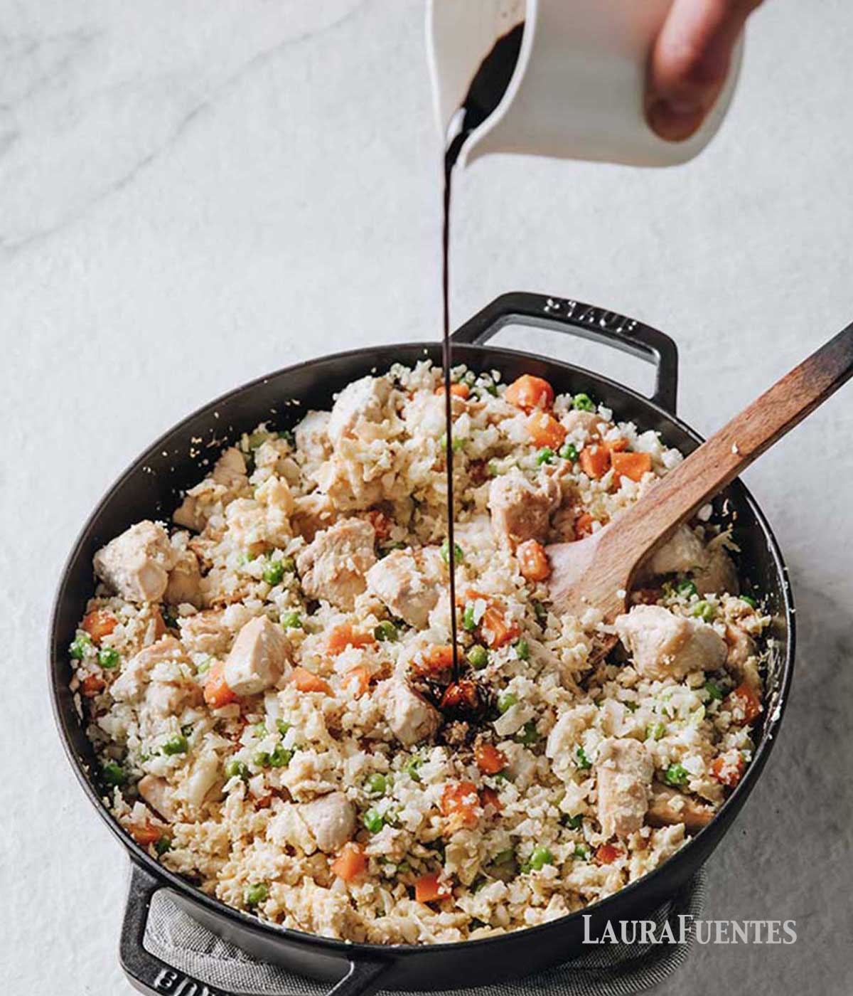 soy sauce being poured into skillet filled with chicken cauli fried rice. overhead view of skillet filled with healthy chicken fried rice.
