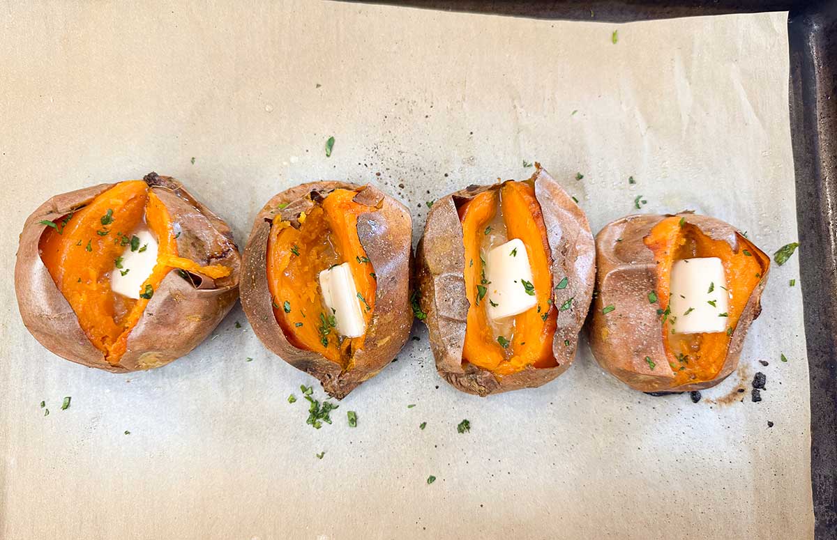 four baked sweet potatoes split in half topped with butter.