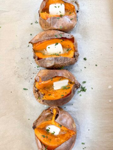 four baked sweet potatoes split in half topped with butter.