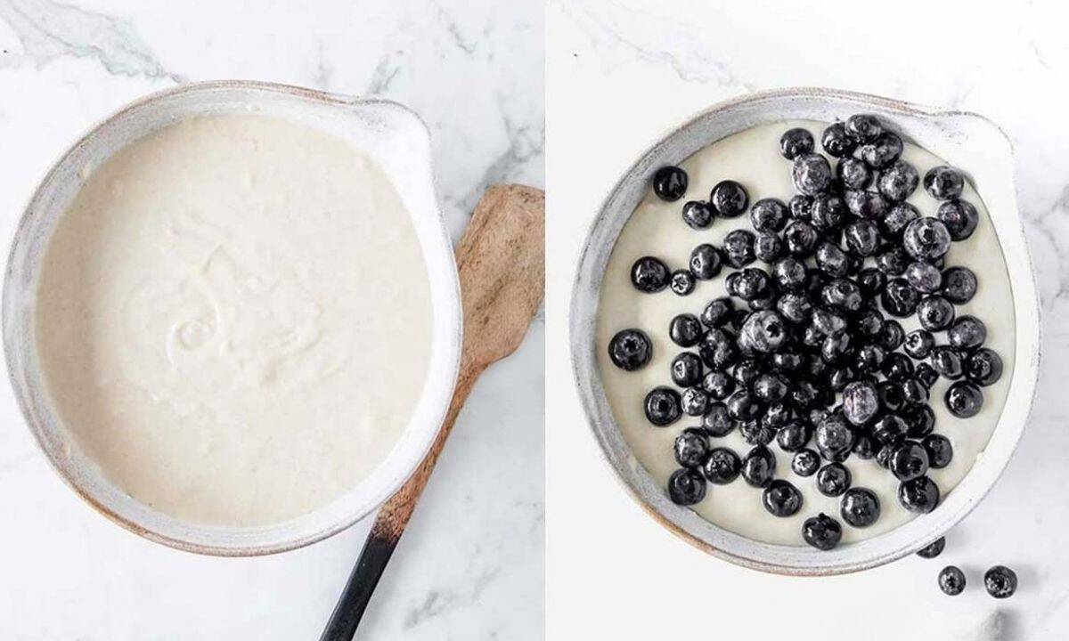 on the left: large white bowl filled with breakfast bread batter. Wooden spatula to one side of bowl, on the right: large bowl of breakfast bread batter with blueberries poured over the top. Some blueberries spilled onto the countertop.
