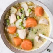 overhead view of a creamy chicken stew with carrots and peas in a bowl with a spoon in it that was made in the crockpot
