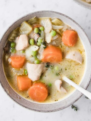 overhead view of a creamy chicken stew with carrots and peas in a bowl with a spoon in it that was made in the crockpot