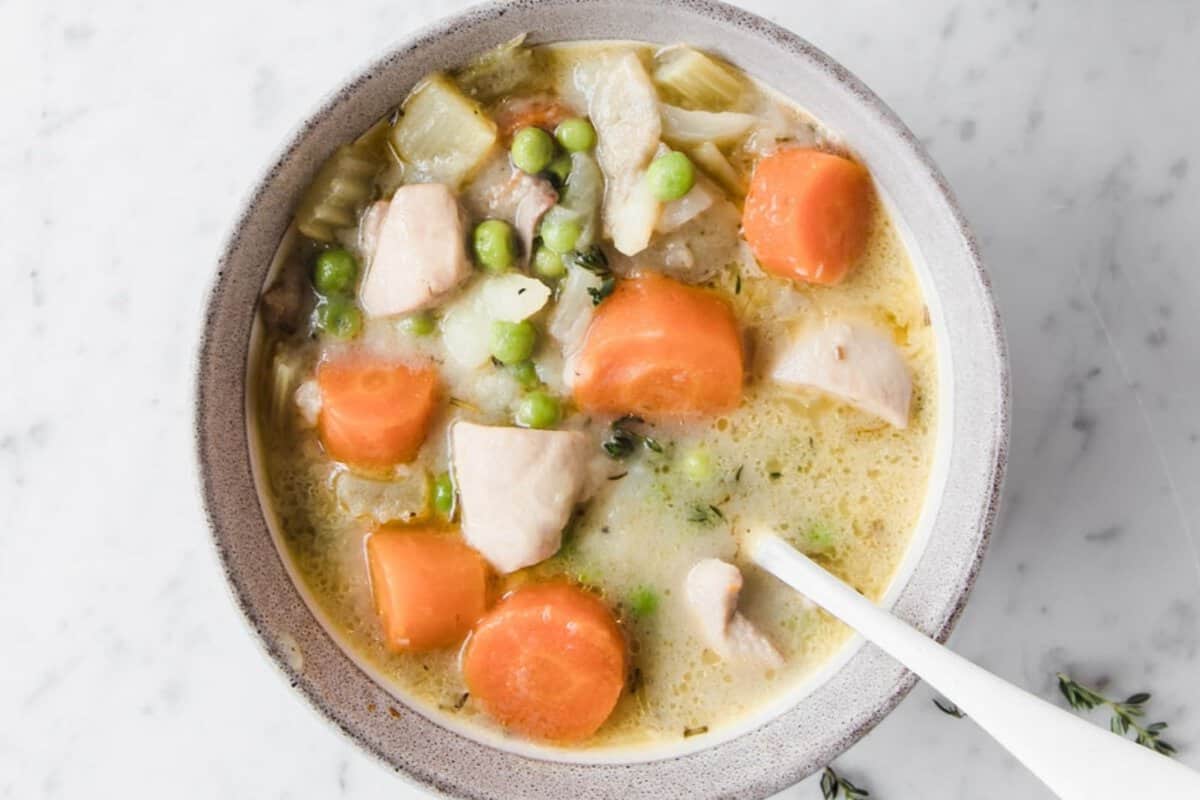 overhead view of a creamy chicken stew with carrots and peas in a bowl with a spoon in it