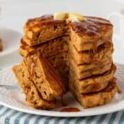 front view of a stack of healthy pumpkin pancakes sliced on a plate topped with butter and syrup. they're fluffy and great looking.