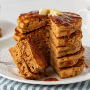 front view of a stack of healthy pumpkin pancakes sliced on a plate topped with butter and syrup. they're fluffy and great looking.