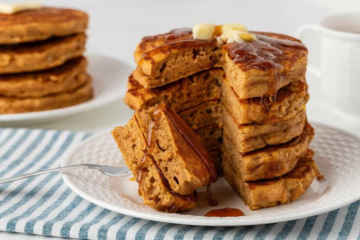 front view of a stack of healthy pumpkin pancakes sliced on a plate topped with butter and syrup. they're fluffy and great looking. 