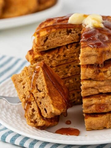 front view of a stack of healthy pumpkin pancakes sliced on a plate topped with butter and syrup. they're fluffy and great looking.
