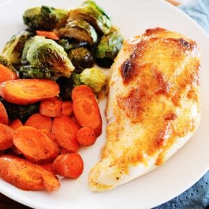 one chicken breast on a white plate with sliced vegetables to the side.