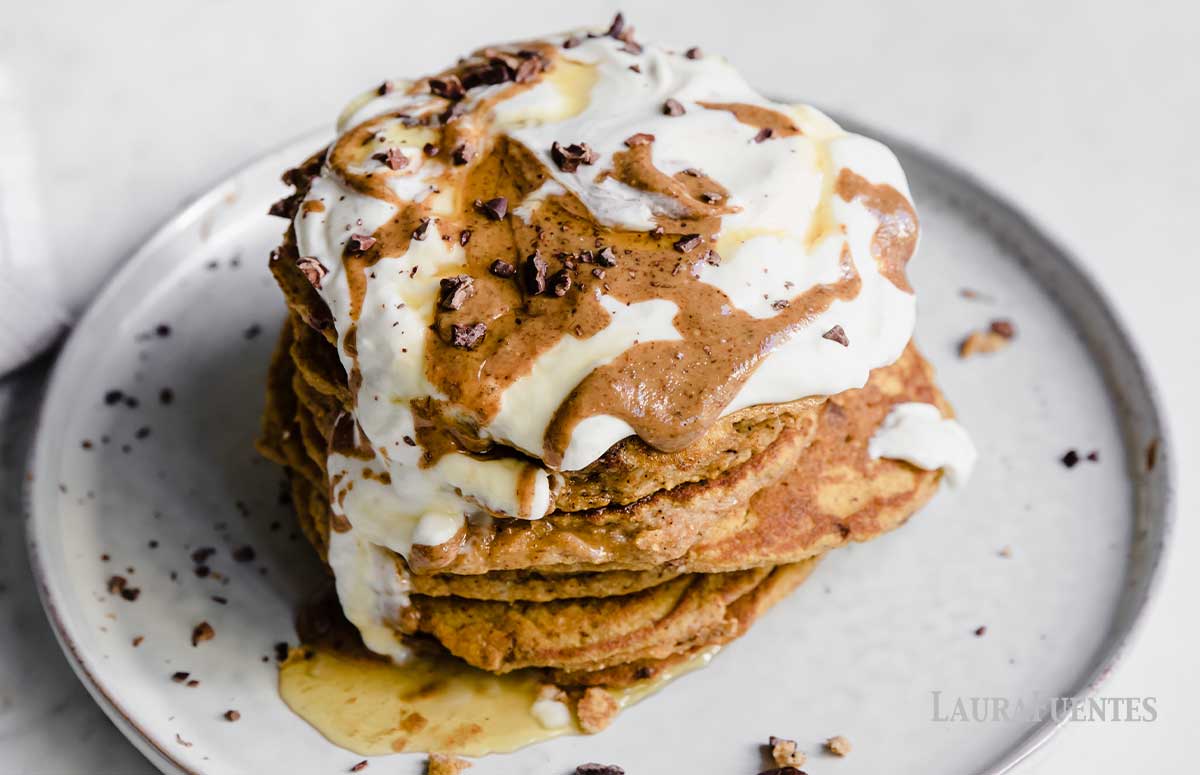 two plates of pumpkin spice pancake stacks, topped with whipped cream, syrup and chocolate.
