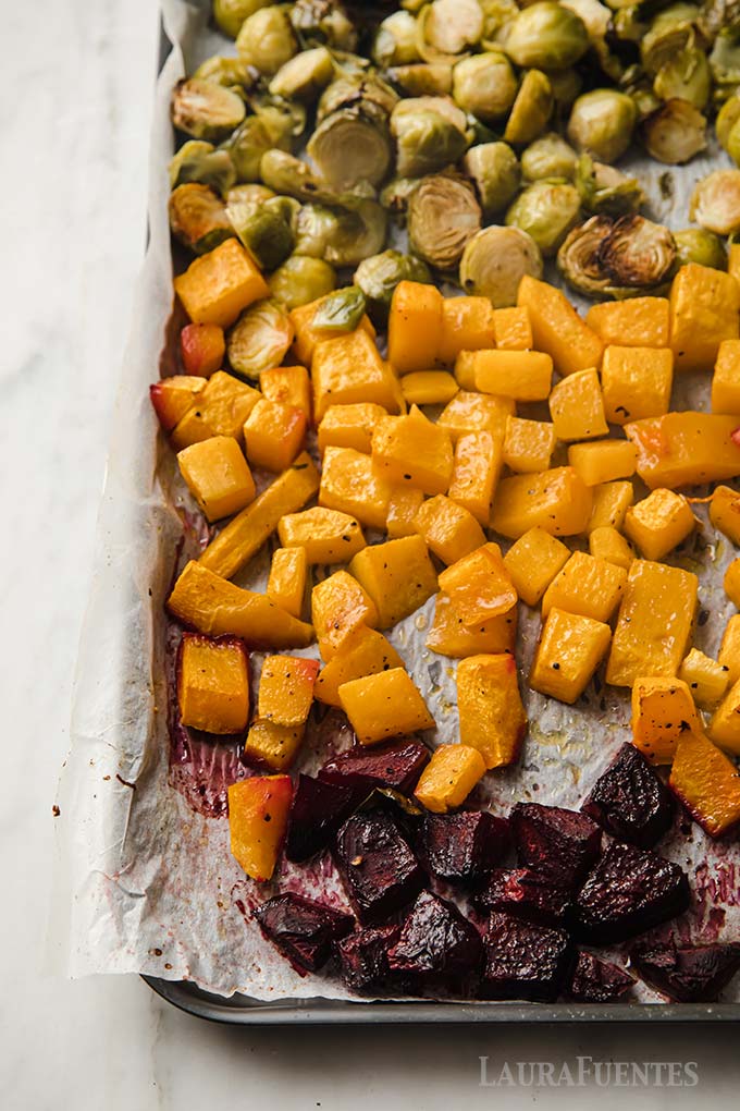 part of a baking sheet filled with chopped beets, butternut squash and halved Brussels sprouts, all roasted.