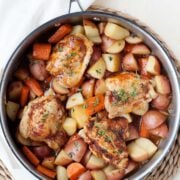 image: large skillet filled with cooked potato chunks, carrot chunks and chicken thighs.