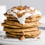large stack of pumpkin spice pancakes topped with whipped cream and syrup