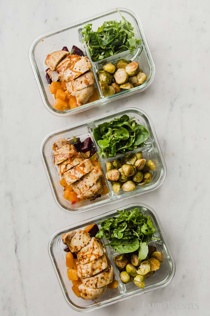 three lunch prep containers with sliced chicken, roasted vegetables and salad greens