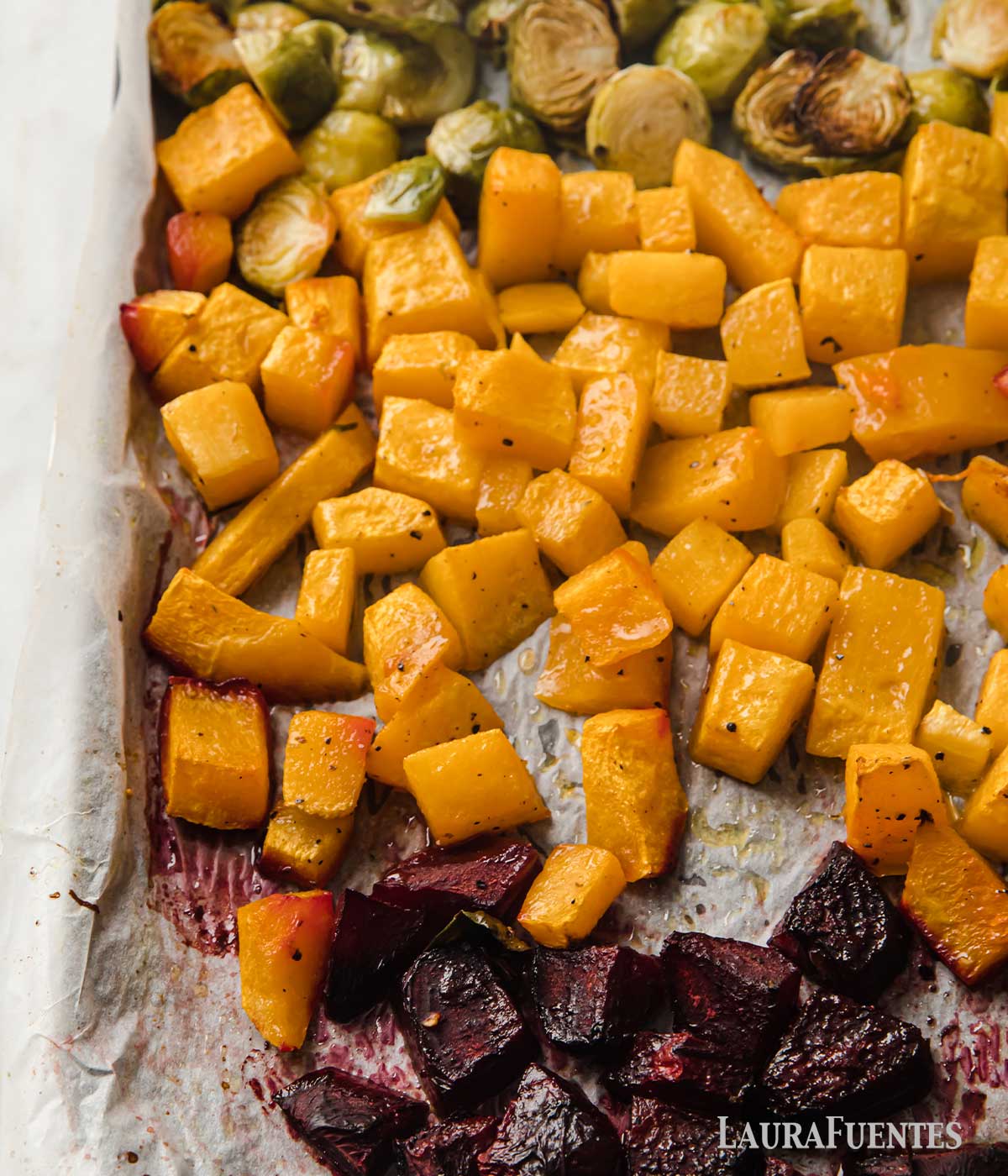 part of a baking sheet filled with chopped beets, butternut squash and halved Brussels sprouts, all roasted.
