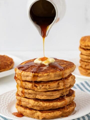 fluffy stack of sweet potato pancakes on a plate topped with butter pouring maple syrup over the top