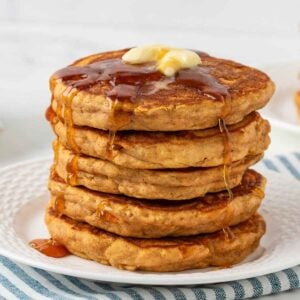 stack of fluffy sweet potato pancakes on a white plate topped with butter and pancake syrup