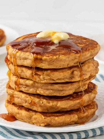 stack of fluffy sweet potato pancakes on a white plate topped with butter and pancake syrup
