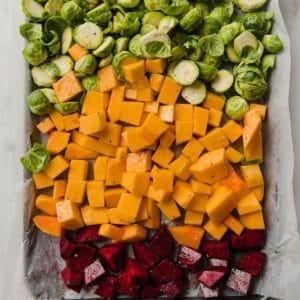a baking sheet filled with chopped beets, butternut squash and halved Brussels sprouts.