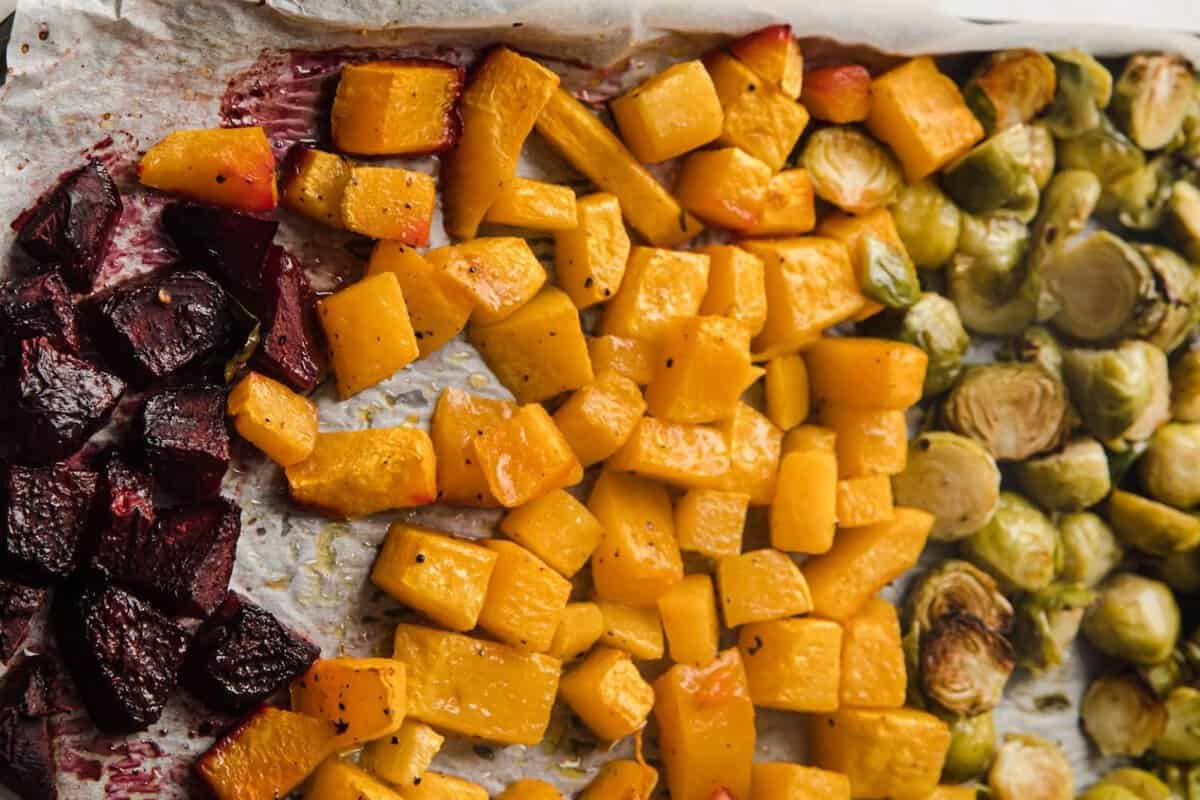 part of a baking sheet filled with roasted chopped beets, butternut squash and halved Brussels sprouts, all roasted.