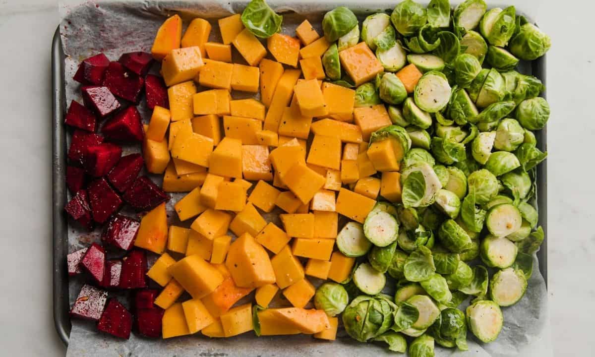 a baking sheet filled with chopped beets, butternut squash and halved Brussels sprouts
