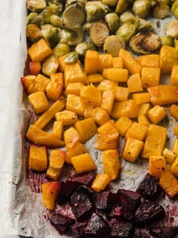 part of a baking sheet filled with roasted chopped beets, butternut squash and halved Brussels sprouts, all roasted.